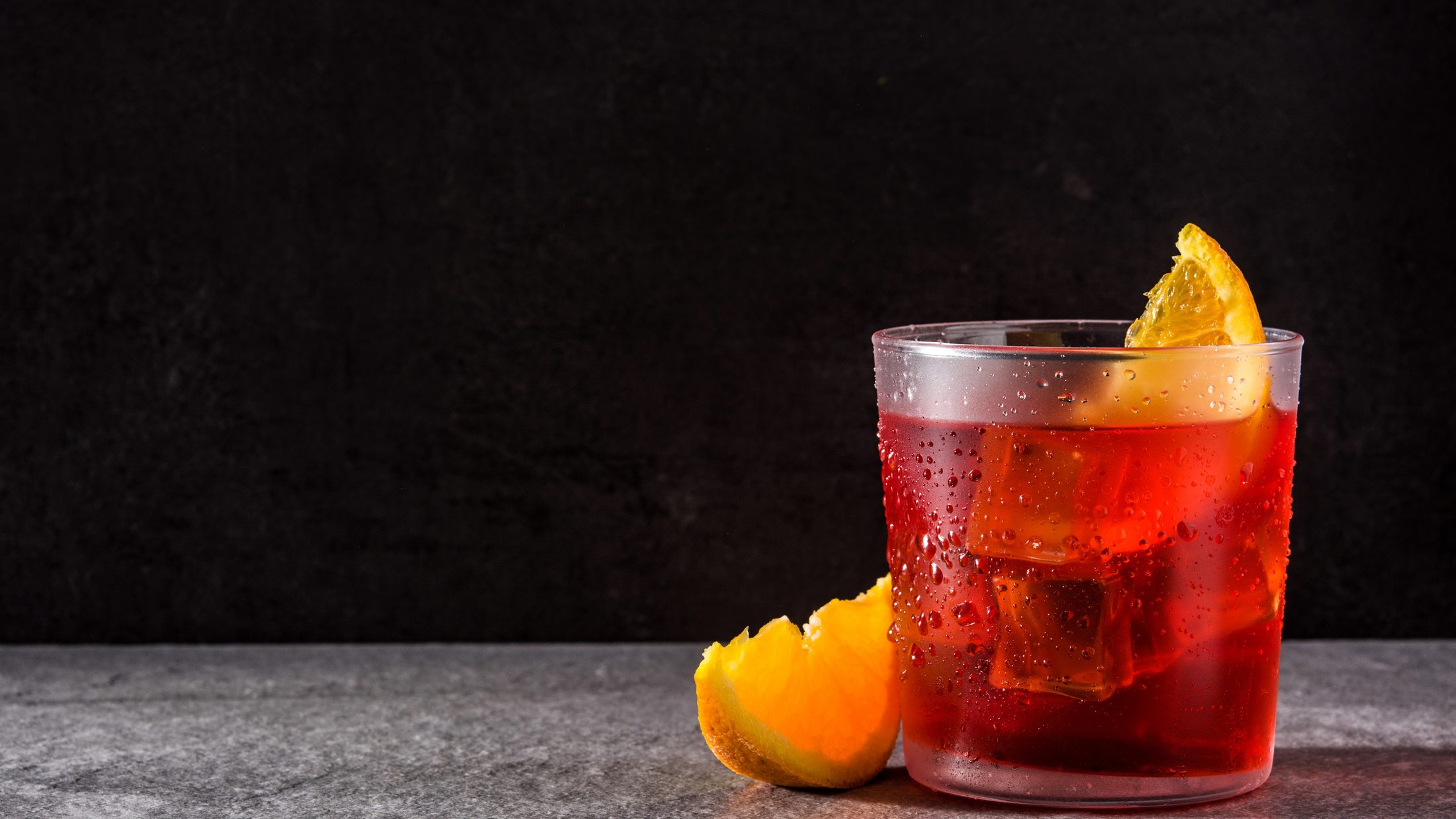 Cóctel servido con hielo y naranja sobre una barra oscura